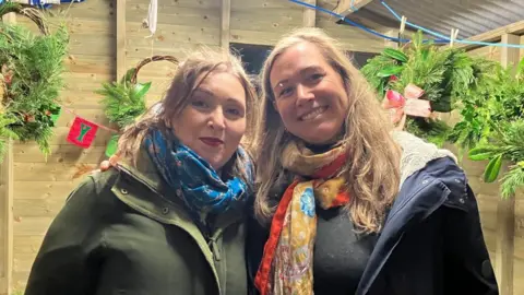 Froach Ferguson (left) wearing a blue scarf and green jacket and Annie Buchanan (Right) is wearing a yellow and orange scarf with blue jacket. Froach has shoulder-length brown hair and Annie has longer blonde hair.