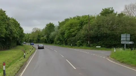 A google maps image showing a main road with a t-junction to the right and lots of green trees and verges lining the road