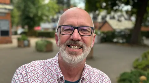 A head and shoulders photograph of Councillor Craig Leyland. He is wearing a white and red shirt.