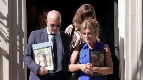 PA Media A man in a dark suit and a woman in a blue dress exit 10 Downing Street. They are carrying framed photos of their children.