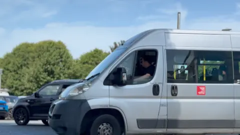 A grey minibus in a carpark.