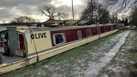 A cream coloured narrowboat with painted red sections on a canal with icy grass on the towpath beside