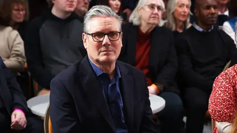 Getty Images Keir Starmer sitting and looking serious, staring into middle distance in a room with general public in Hastings 