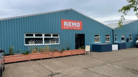 John Devine/BBC The outside of a light blue building with cladding metal cladding and two apex roofs. The sign above the door reads "Reno".