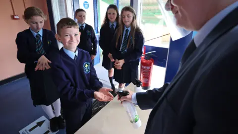 PA Media A principal in West Belfast uses sanitiser on pupils hands, as schools in Northern Ireland reopen to pupils following the coronavirus lockdown, 24 August 2020