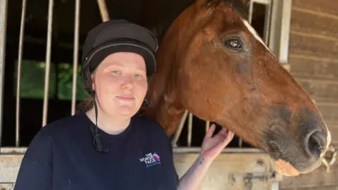 BBC A woman and a brown horse in a stable