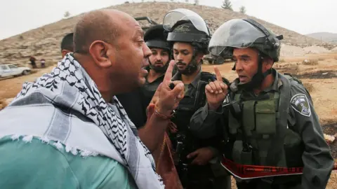 Reuters A Palestinian protester argues with an Israeli border policeman near Hebron in the occupied West Bank (15 November 2019)