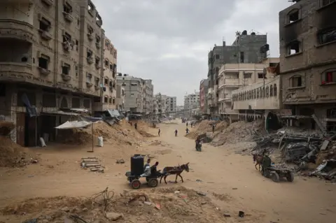 AFP Palestinians walk between damaged buildings in Khan Yunis in the southern Gaza Strip on May 2, 2024, amid the ongoing conflict between Israel and the Hamas movement.