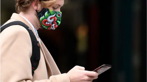 Getty Images Woman looking at her phone and wearing a mask