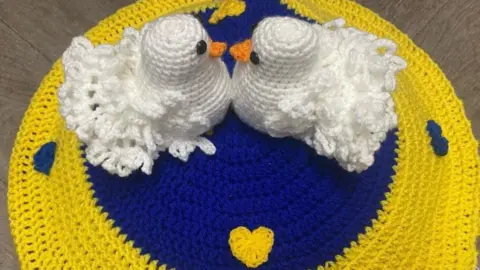 The Secret Yarn Bomber Crochet tribute to Ukraine showing two doves on a blue and yellow background