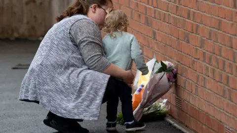 PA Media A woman and child laying flowers