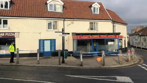 Steve Silk/BBC Police officer guarding crime scene with police tape in foreground.