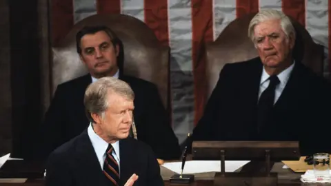 Wally McNamee Speaker of the House "Tip" O'Neill watches as US President Jimmy Carter speaks