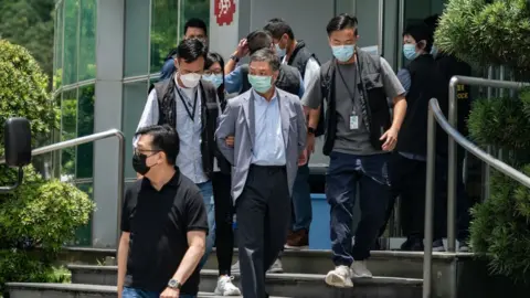 Getty Images Chief Operations Officer Chow Tat Kuen (C) is escorted by police from the headquarters of the Apple Daily newspaper