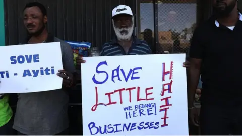 Getty Images A man holding a poster which reads save Little Haiti businesses, we belong here