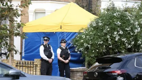 PA Media Police officers outside a house in north London