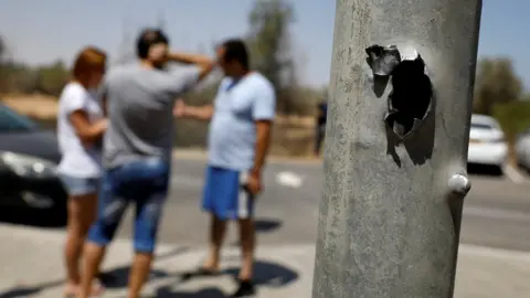 Reuters Israelis stand next to a pole damaged by a rocket fired from the Gaza Strip (20 June 2018)