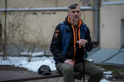 Olexa Sokil, a veteran of the first years of the war in eastern Ukraine, is seen sitting on a bench holding a walking stick