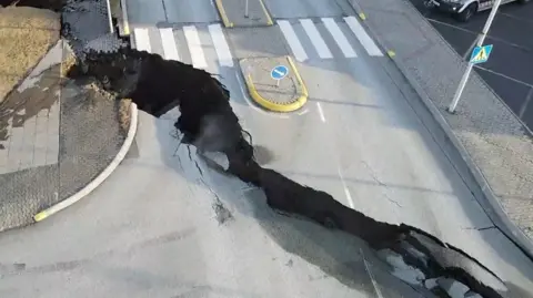 Huge crack running across road in Iceland next to pedestrian crossing