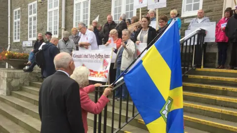 BBC Campaigners carrying the Pembrokeshire flag before the health board meeting