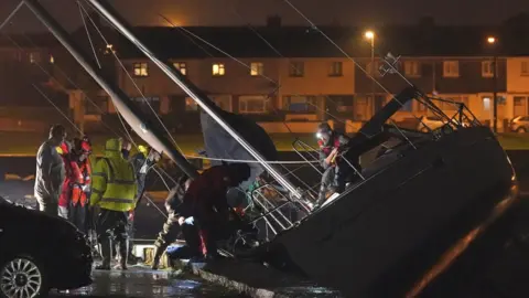 PA Media Members of the Coast Guard inspect the damage to a boat after it broke free from its berth and crashed into the harbour during Storm Betty in Dungarvan, County Waterford.