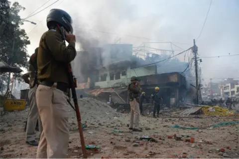 AFP Policemen stand along a road scattered with stones as smoke billows from buildings following clashes between supporters and opponents of a new citizenship law, at Bhajanpura area of New Delhi on February 24, 2020