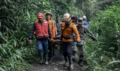 EPA A group of rescue workers carrying a survivor amid foliage, in Agam West Sumatra on 4 December