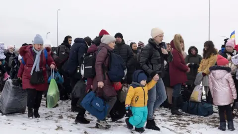 Getty Images Refugees fleeing conflict make their way to the Krakovets border crossing with Poland