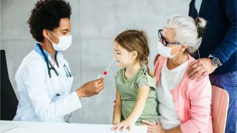 Getty Images A little girl having a PCR test, together with her family