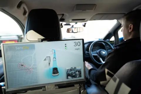 PA Media A shot inside a car with a screen showing the computer's view of the car, and a driver whose hands are off the steering wheel
