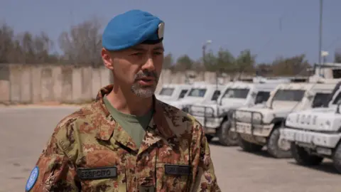 Colonel Alberto Salvador standing in front of a row of white UN trucks