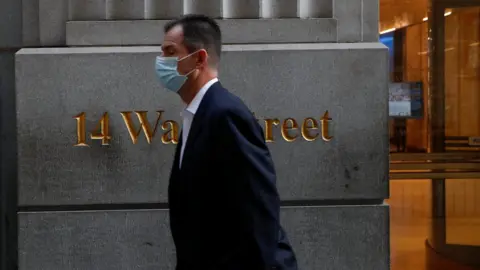 Reuters man wearing a protective face mask walks by 14 Wall Street, as the global outbreak of the coronavirus disease (COVID-19) continues, in the financial district of New York, U.S., November 19, 2020