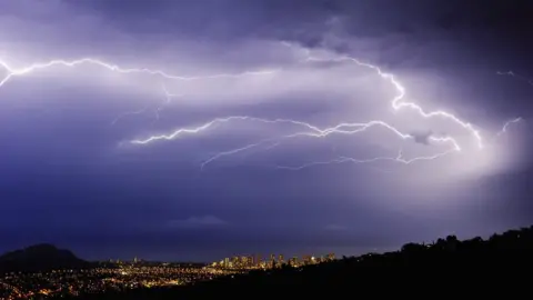Science Photo Library Lightning bolts over a city in a valley at night
