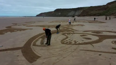 PA Media People creating a sand drawing