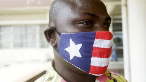 EPA A man wears a mask decorated in the colour and pattern on Liberia's national flag on 27 April.