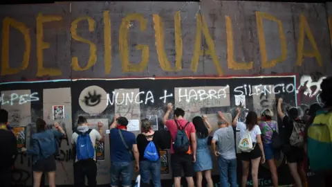 AFP People demonstrate under graffiti reading "Inequality" during a protest demanding greater social reforms from Chilean President Sebastian Pinera in Santiago on 12 November, 2019.