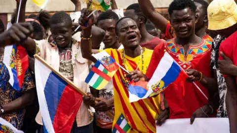 Getty Images Russian and Central African Republic flags are waived by demonstrators gathered in Bangui on March 5, 2022 during a rally in support of Russia