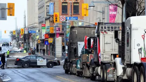 Getty Images A line of trucks parks on a road in downtown Ottawa with police nearby during anti-vaccine mandate protests earlier this year.