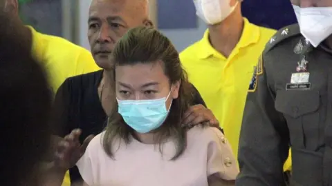 EPA Police escort a masked Sararat Rangsiwuthaporn