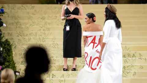 Getty Images Alexandra Ocasio-Cortez wearing a white formal dress with the words "Tax the Rich" scrawled in red on the back