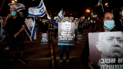 Reuters People hold up posters showing Benny Gantz and quoting him as saying: "I would not sit in a government under a man facing criminal indictment" at a protest in Tel Aviv on 19 April 2020