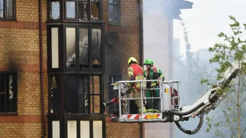 PA Media Fire crews continue spraying water into the block of flats