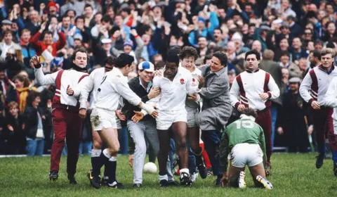 Getty Images England wing Chris Oti (c) is congratulated by captain Will Carling (l) and spectators after scoring three trys in a 35-3 win over Ireland in the Five Nations match at Twickenham on March 19, 1988 in London, England.