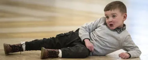 PA Media Dáithí Mac Gabhann poses lying on the floor of the Great Hall of Parliament House in Stormont.