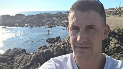 Facebook James Watson photographed in front of a beach