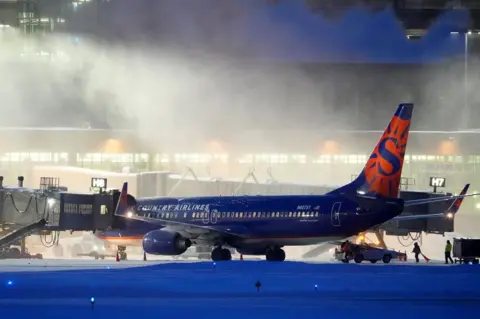 Star Tribune via Getty Images High winds whip around 7.5 inches of new snow at Minneapolis-St. Paul International Airport as workers prepare a Sun Country Airlines plane for take-off Thursday, December. 22, 2022.