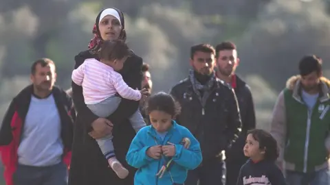 Getty Images Refugee and migrant families walk through the Moria Refugee Camp in 2016