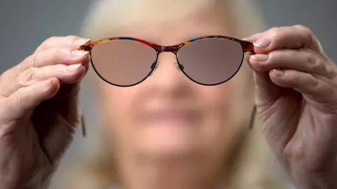 Getty Images Blurred out face of a mature woman holding a pair of glasses with blurred lenses