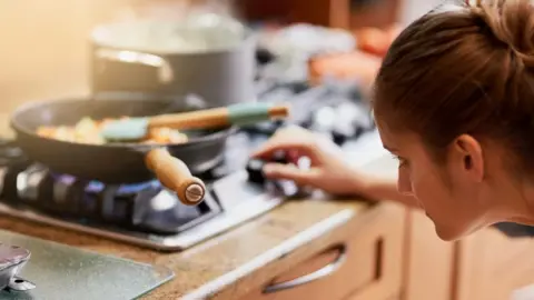 Getty Images Woman adjusting gas hob under pan