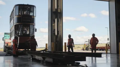 Josh Adam Jones/Science Museum Group An old tram on the back of a truck being eased off by people in safety jackets